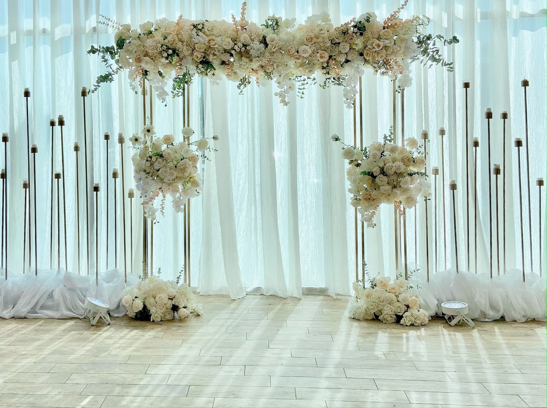 A wedding arch decorated with white flowers and feathers in front of a window.