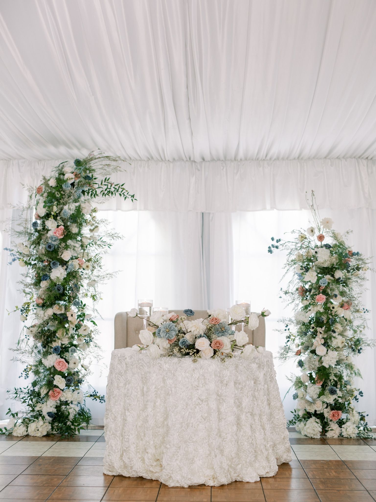 A table with a white tablecloth and flowers on it in a tent.