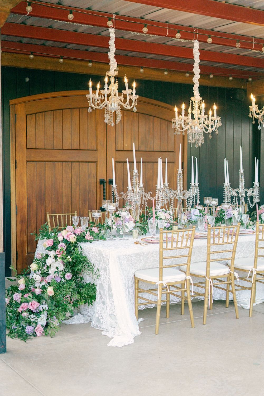 A long table with candles and flowers on it in a room with chandeliers hanging from the ceiling.