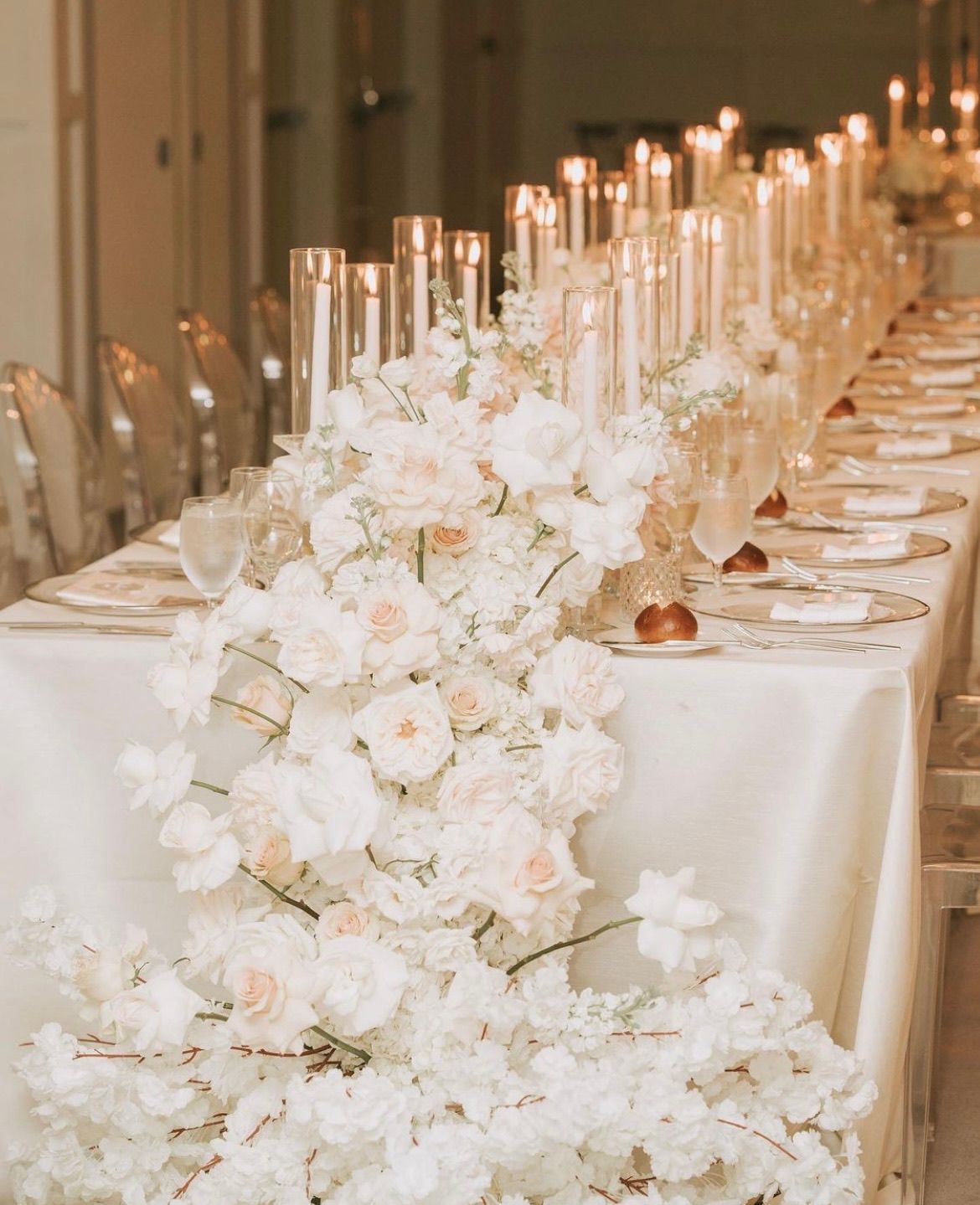 A long table with white flowers and candles on it.