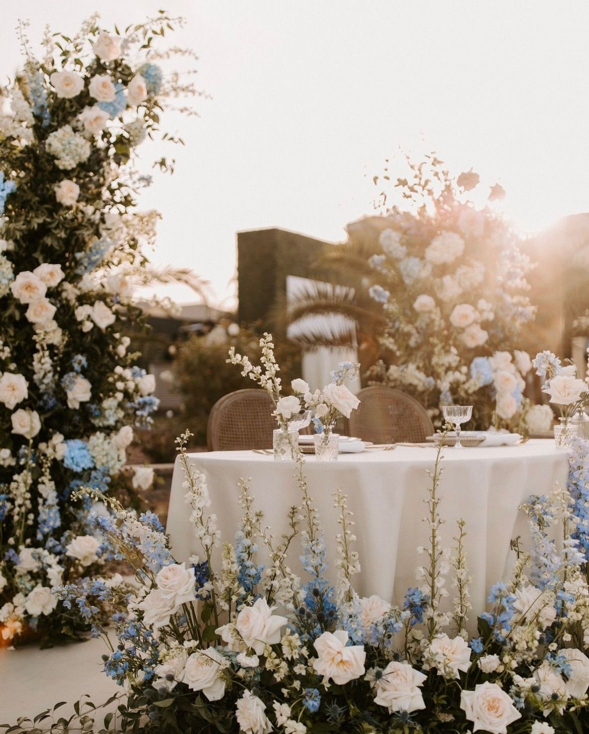 A table with a white table cloth is surrounded by blue and white flowers.