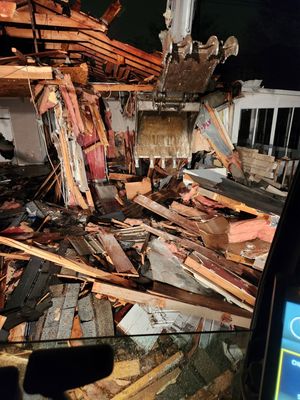 A pile of wood is sitting on the ground in front of a building being demolished.