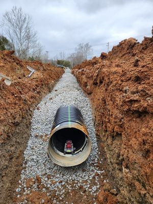 A large pipe is sitting in the middle of a dirt trench.