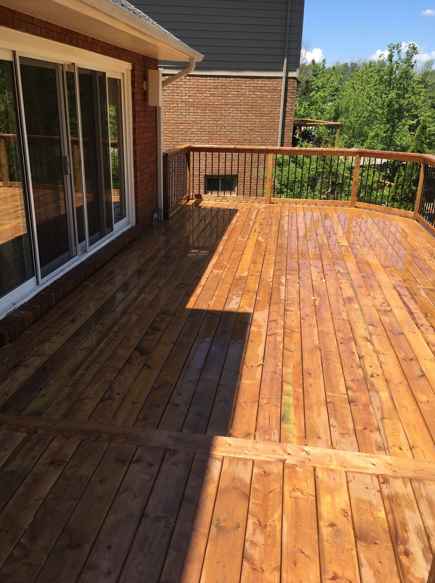 Wooden deck with railing, next to a brick building and sliding glass doors.
