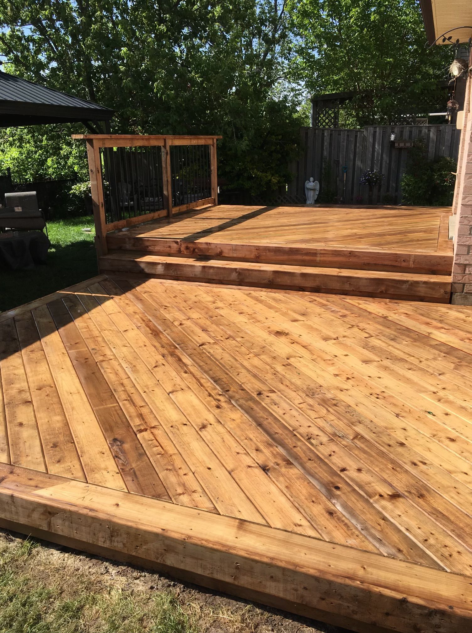 Wooden deck with stairs and railing in a backyard setting. Diagonal plank pattern, brown wood.