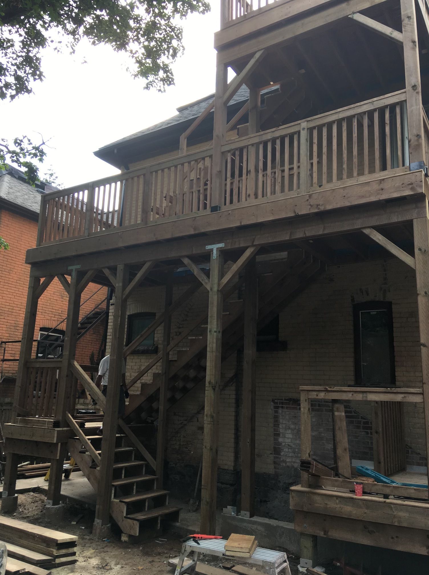 Wooden multi-level deck attached to a brick building with stairs, person, and lumber.