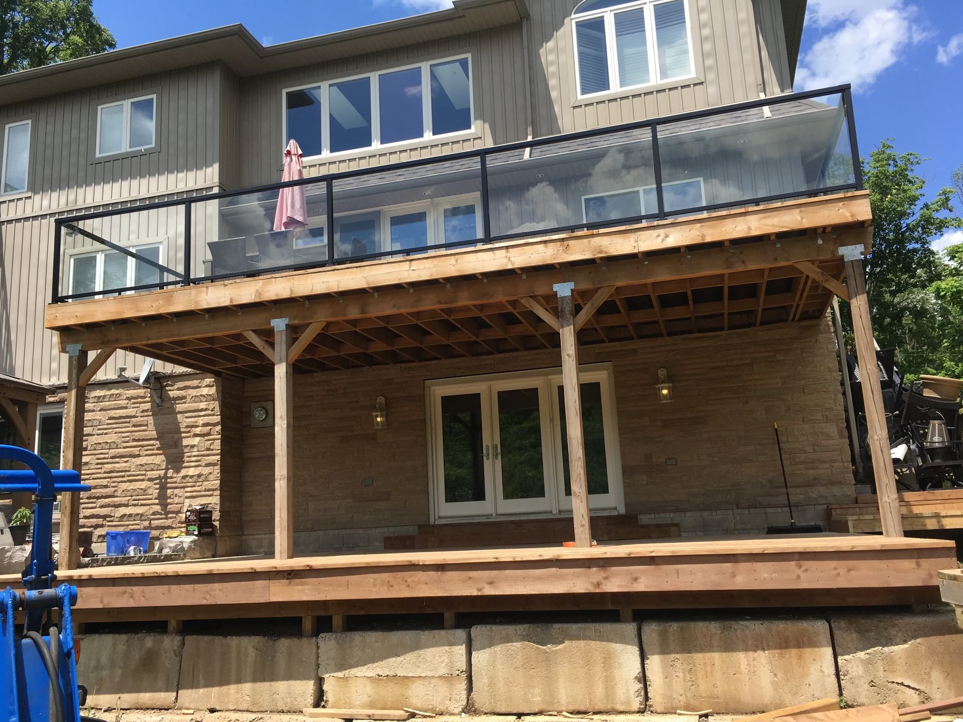 Wooden deck with glass railing attached to a two-story house.
