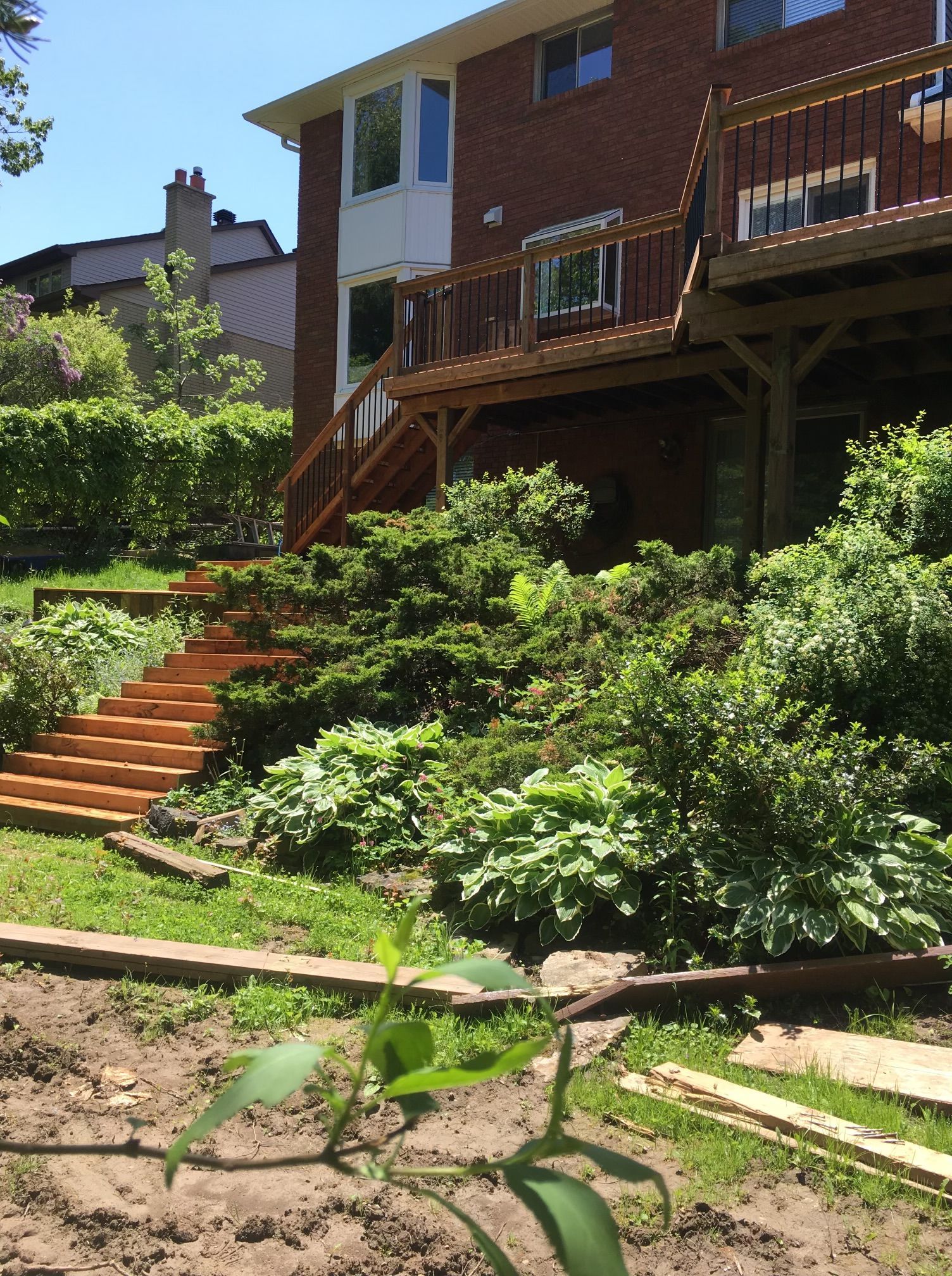 Backyard with a multi-level deck, wooden stairs, and lush green landscaping against a brick house.