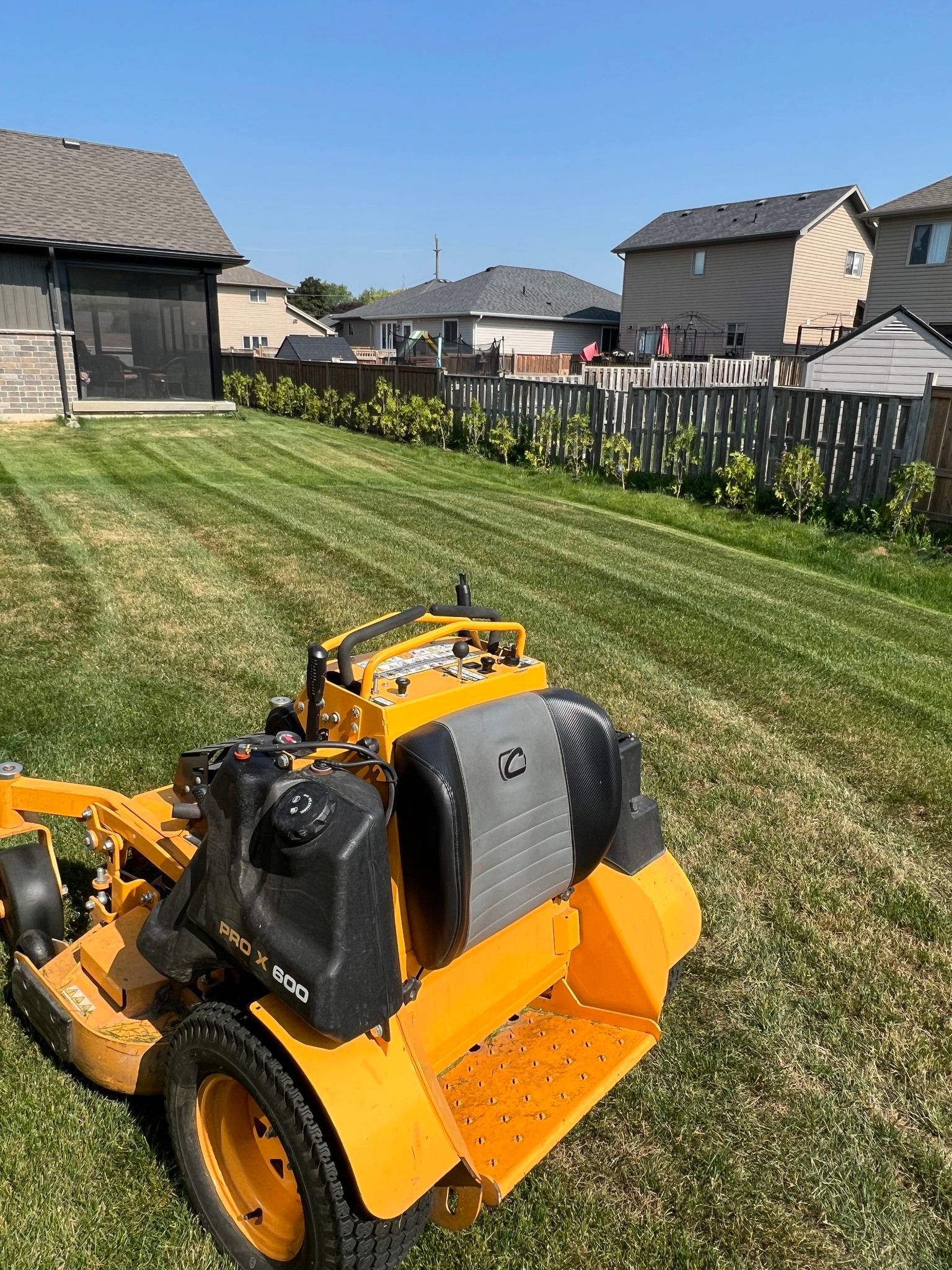 Yellow lawn mower on a green lawn with a house in the background, blue sky.