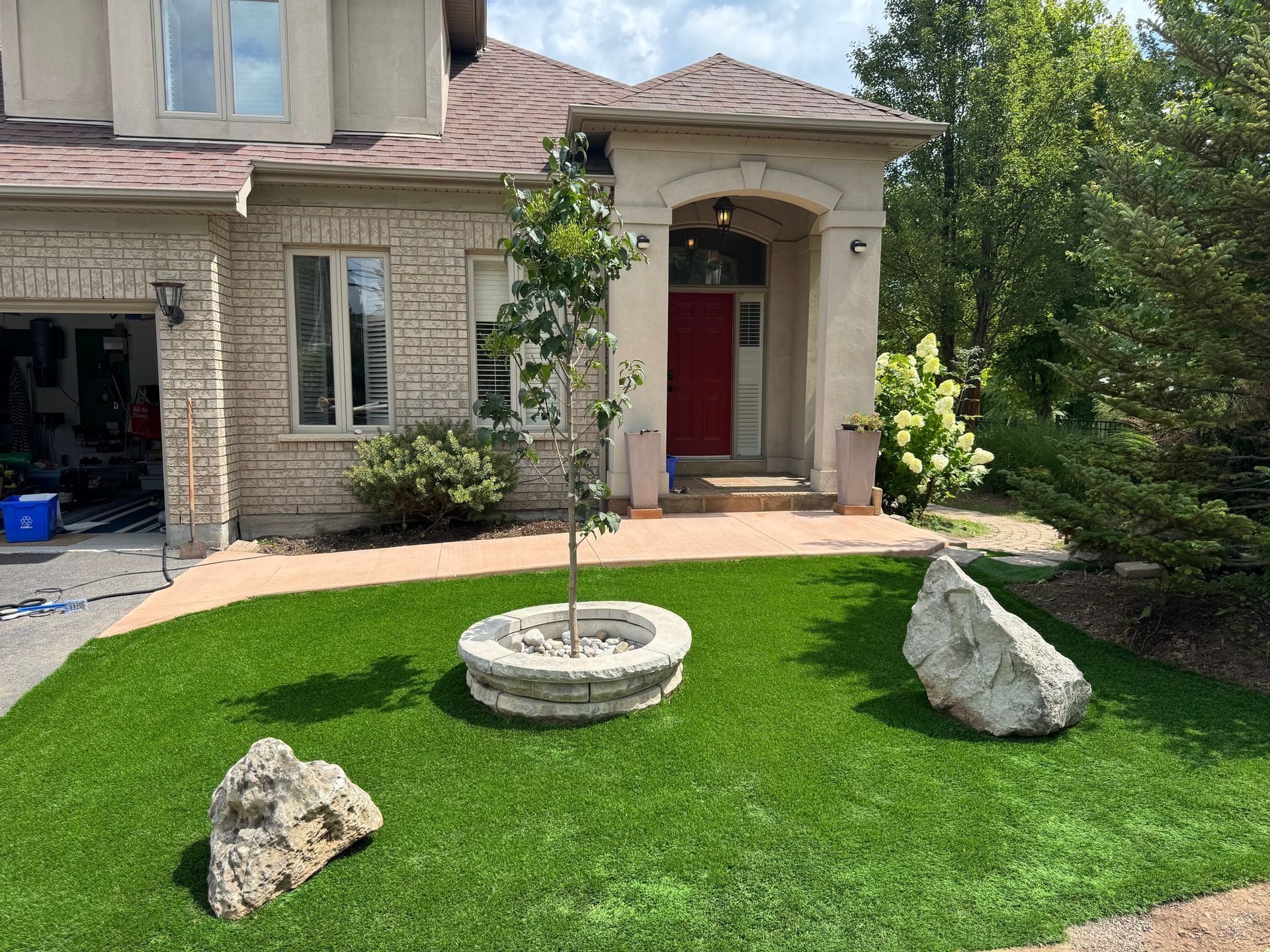 House exterior with artificial green lawn, rock accents, and a red front door.