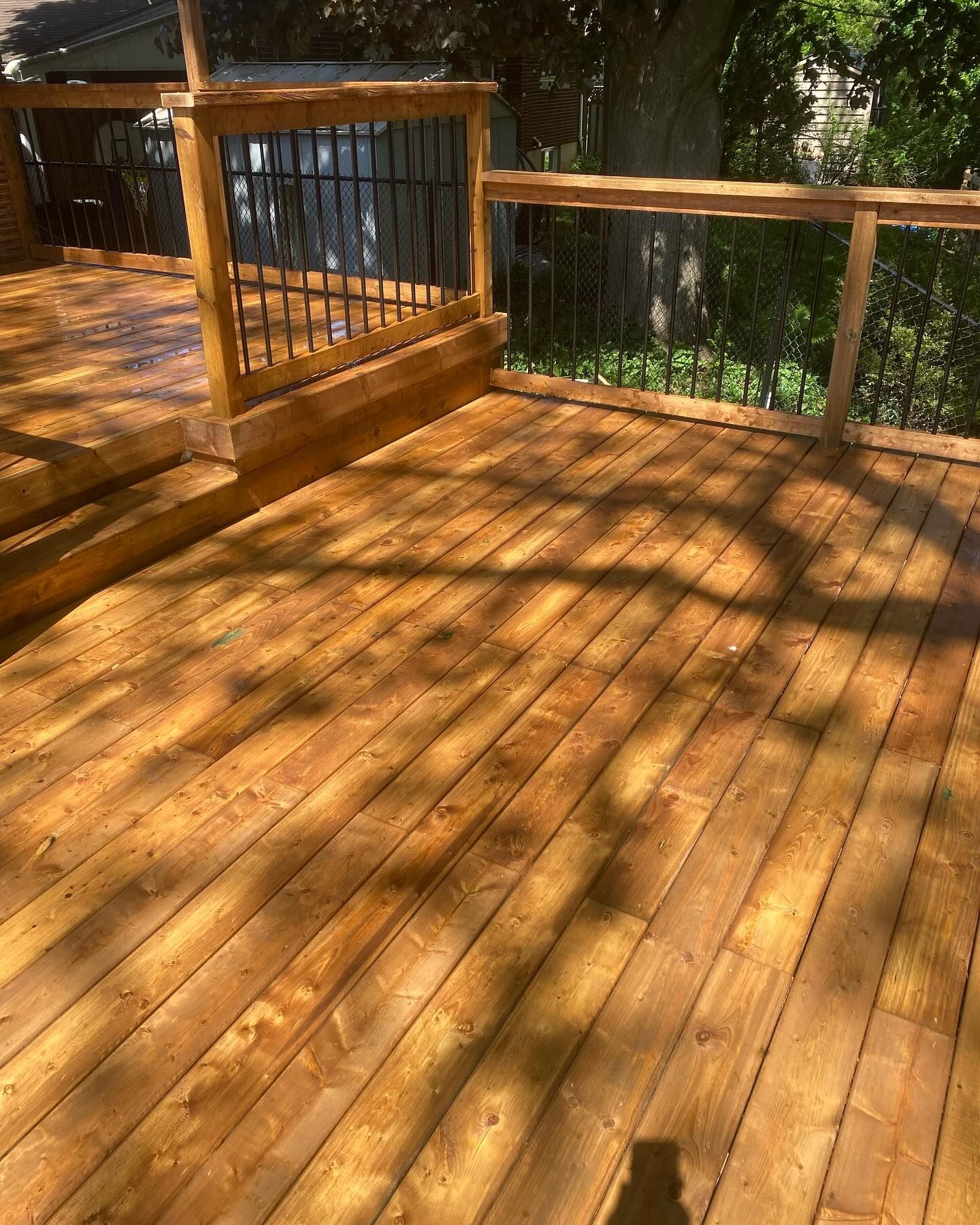 Wooden deck with a railing and black metal bars, bathed in sunlight.