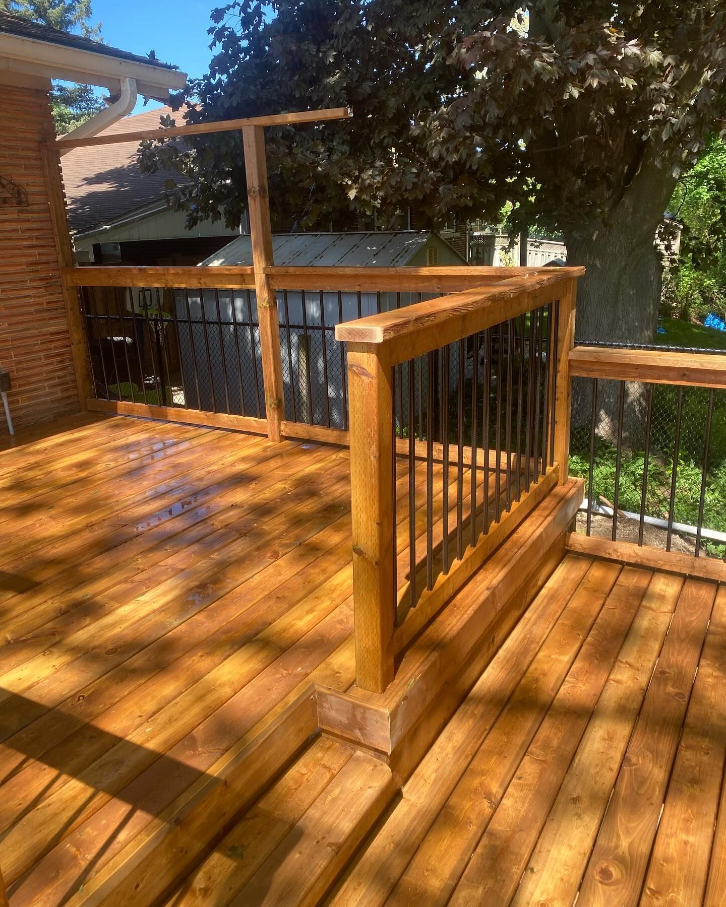 Newly built wooden deck with dark metal railings and bright sunlight.