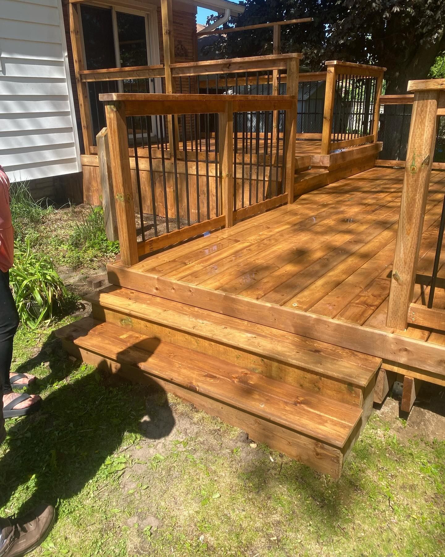 Wooden deck with railing and steps, stained brown, in a grassy backyard.