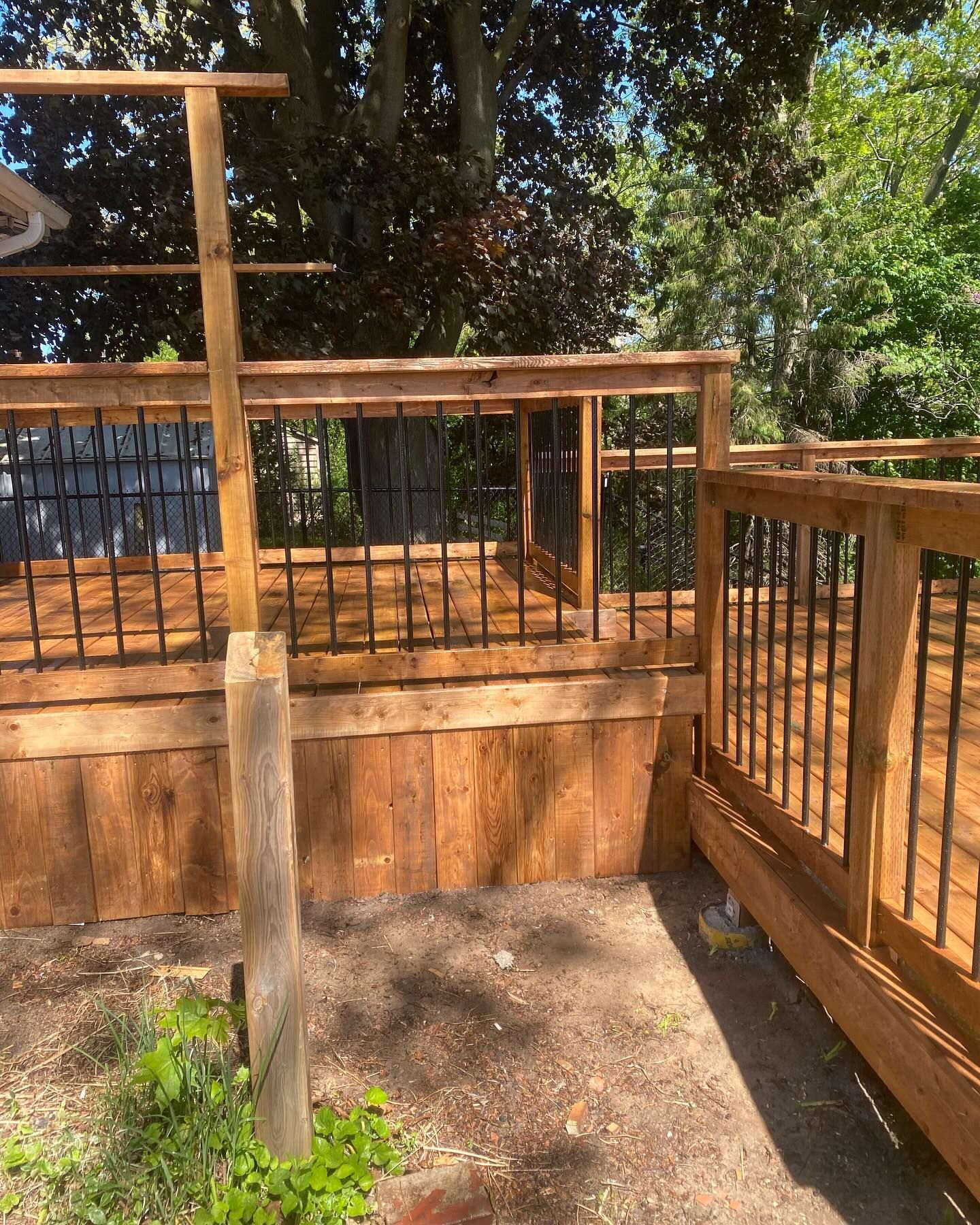 Wooden deck with black railing, brown wood, and green foliage.