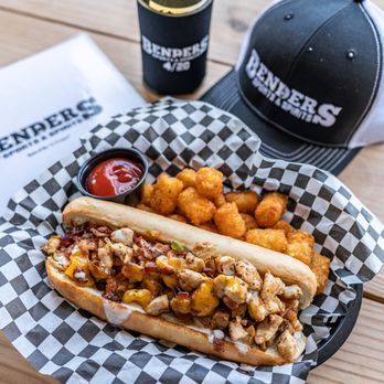 A chicken sandwich is sitting on a checkered paper next to a baseball cap.