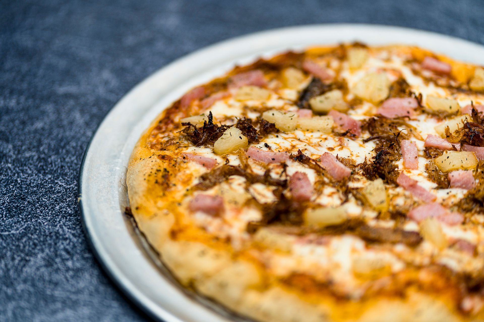 A pizza with ham and pineapple on a white plate on a table.