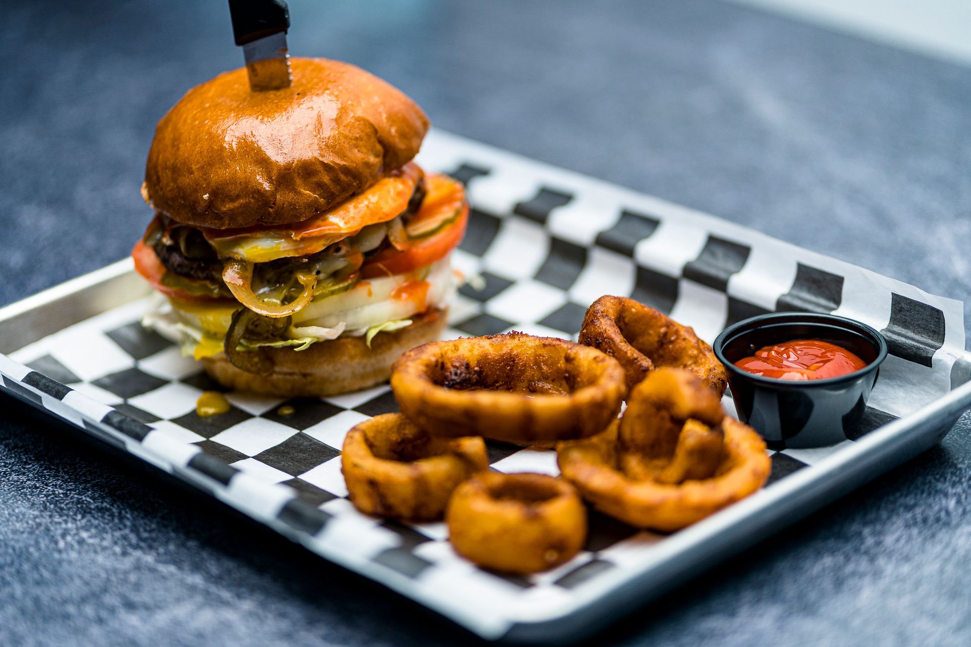 A hamburger and onion rings on a checkered plate on a table.