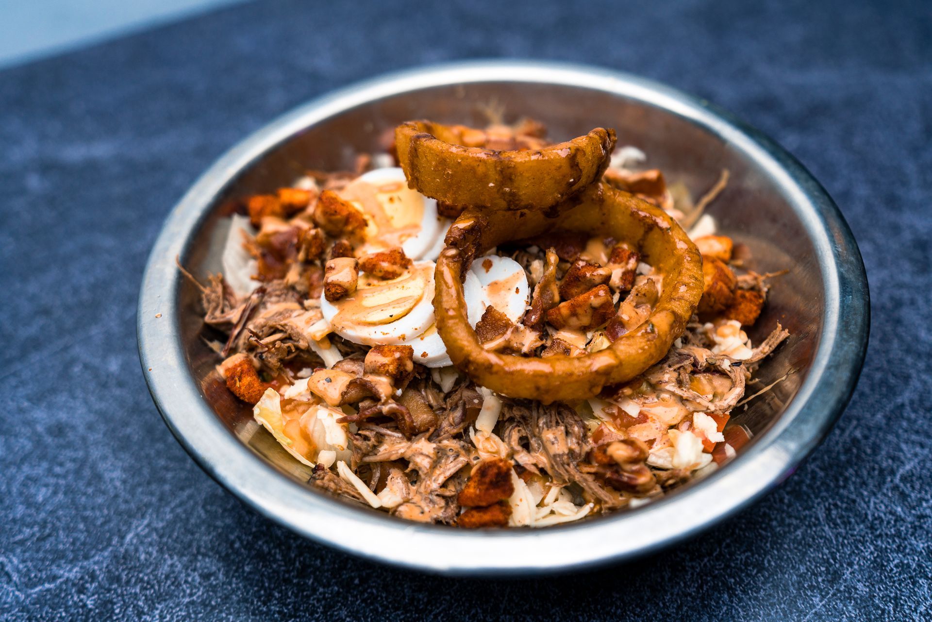 A bowl of food with meat and onion rings on a table.
