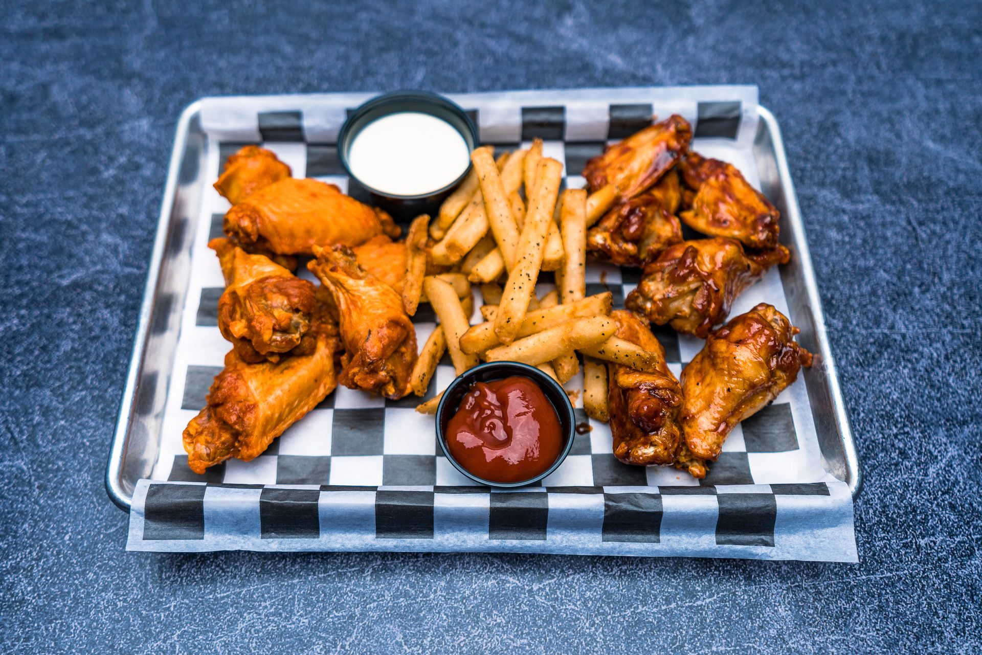 A tray of chicken wings and french fries on a checkered paper.