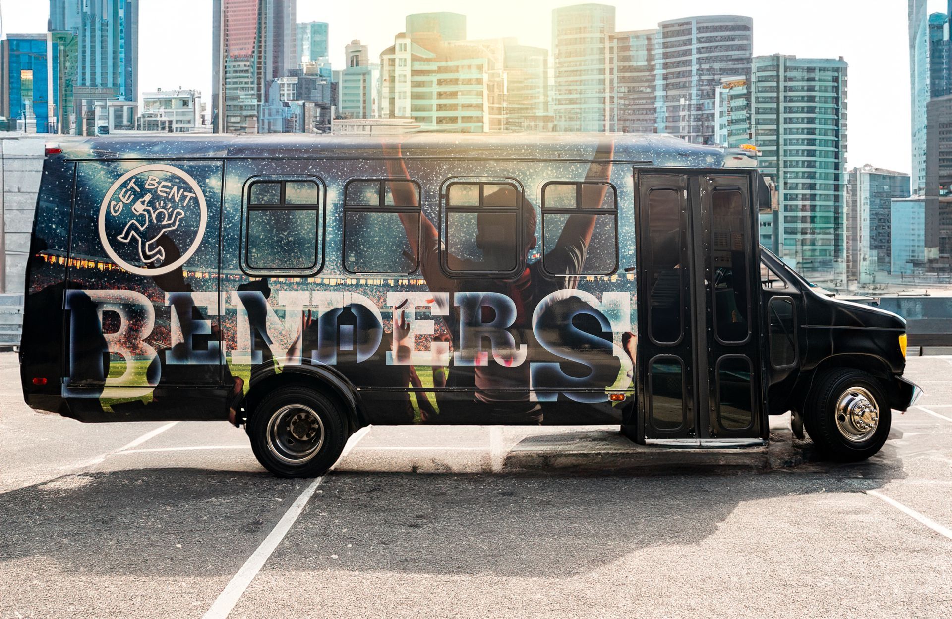 A black bus is parked in a parking lot in front of a city skyline.