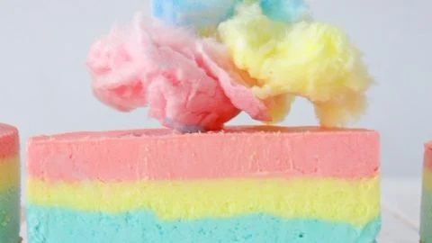A close up of a rainbow colored cake with cotton candy on top.