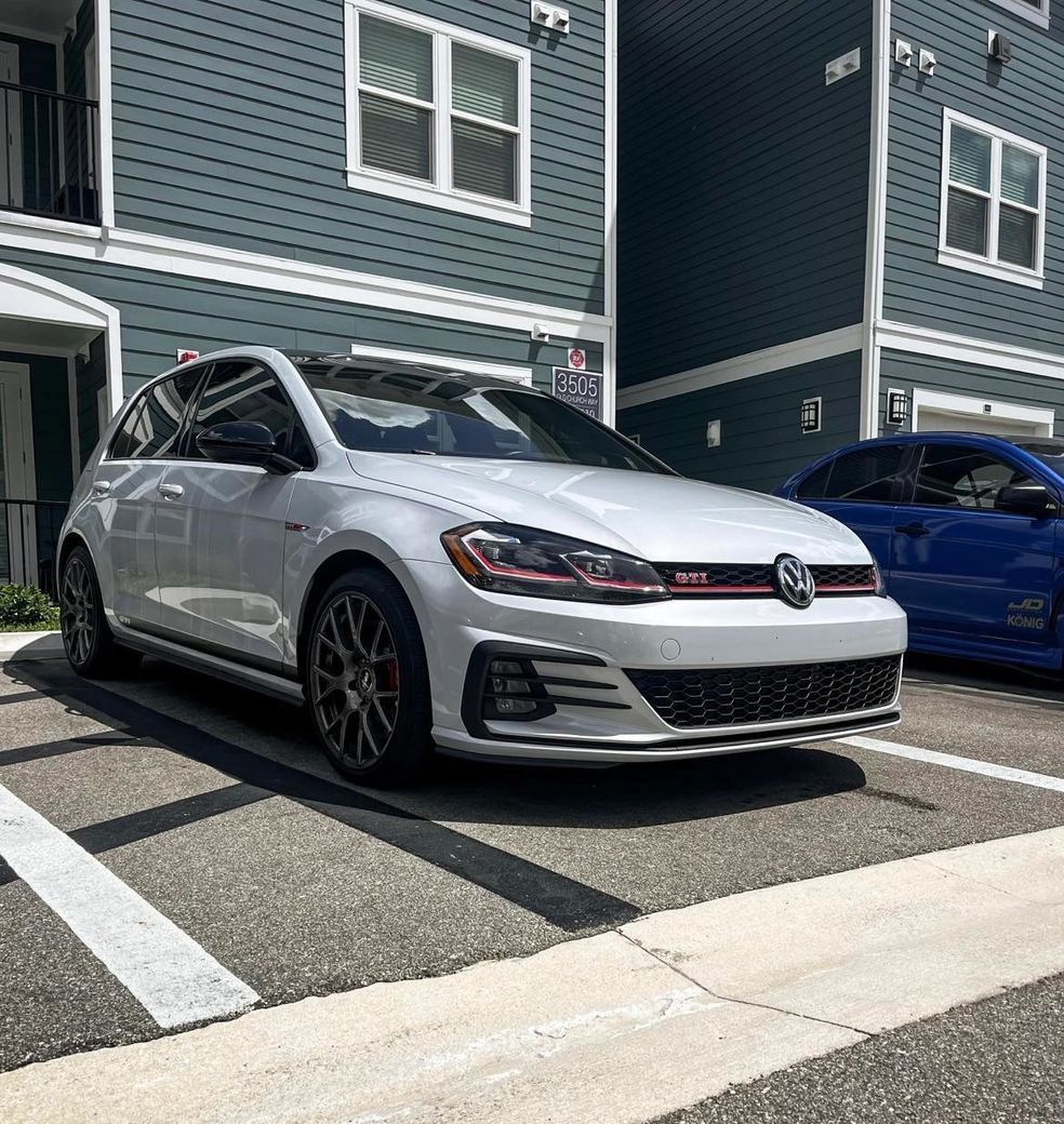 A white car is parked in a parking lot in front of a building.
