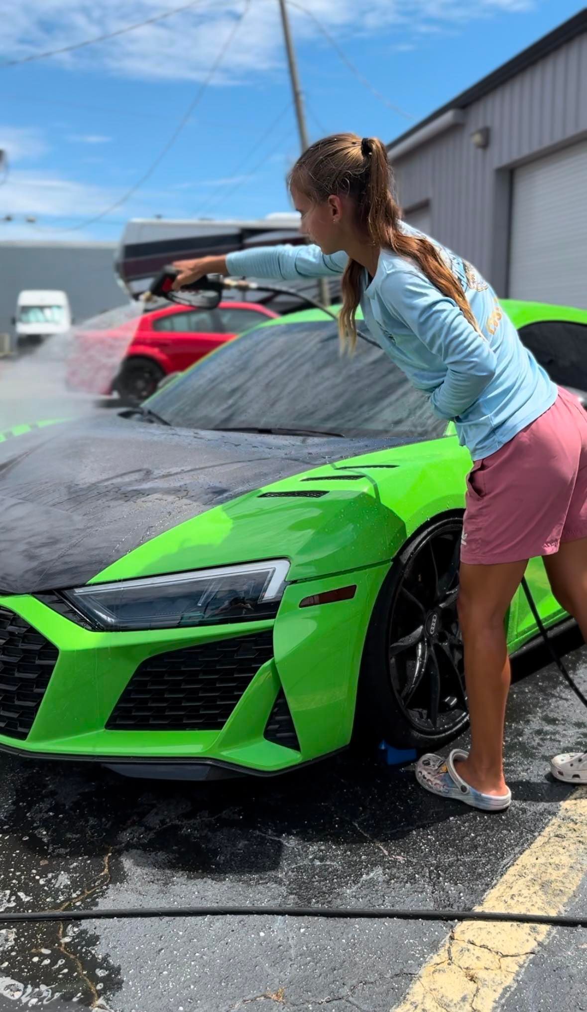 A girl is washing a green sports car in a parking lot.