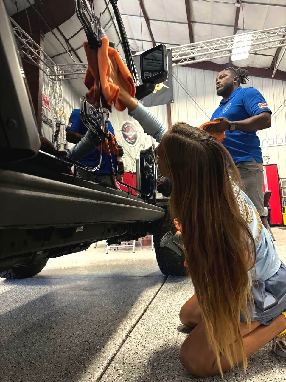 A little girl is kneeling down in front of a car