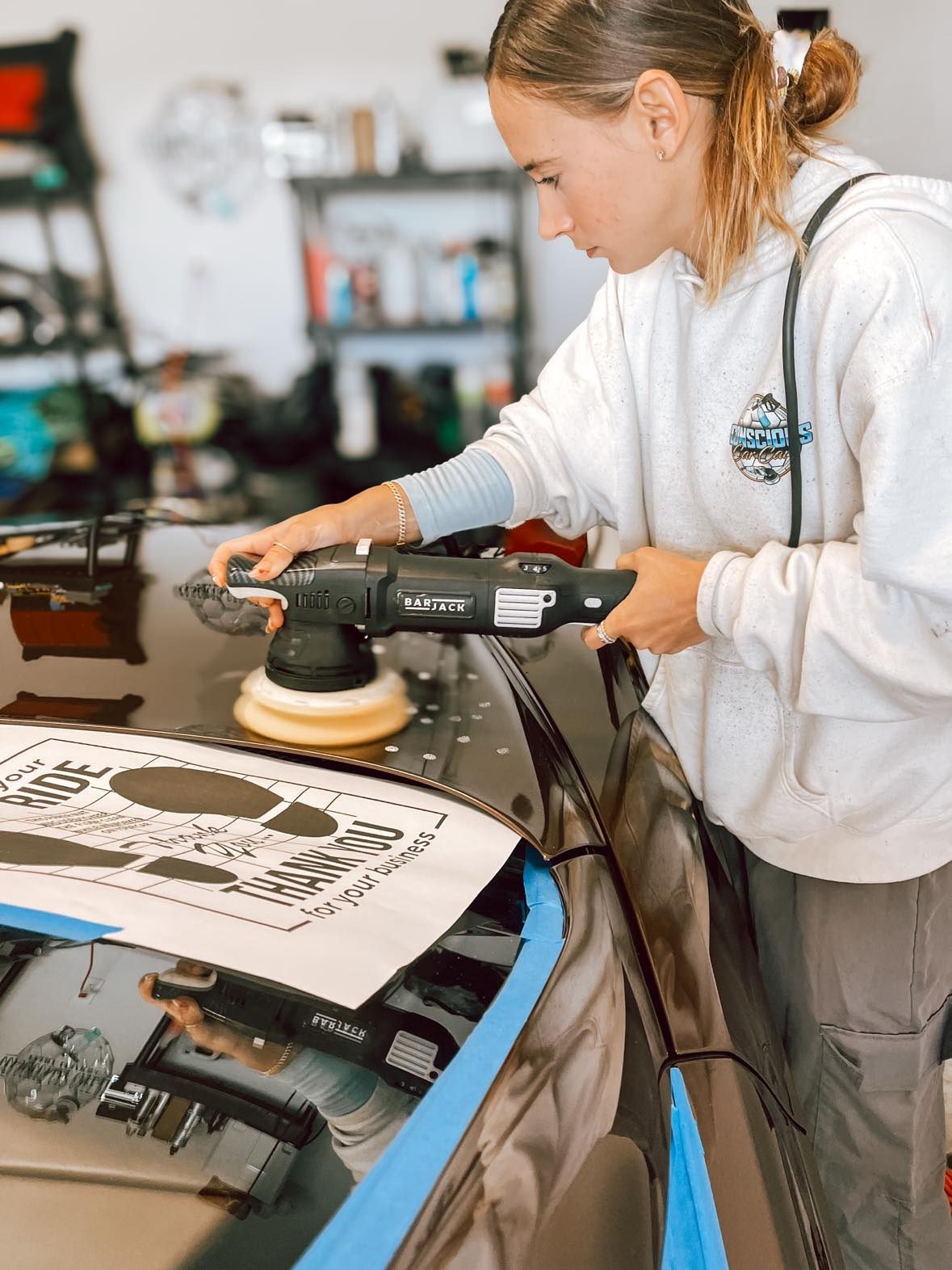 A woman is polishing the hood of a car with a machine.