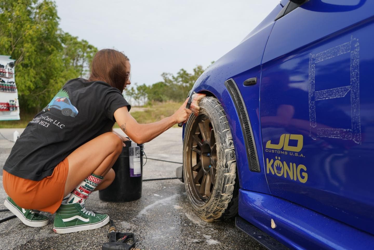 A woman is kneeling down to wash a blue car.