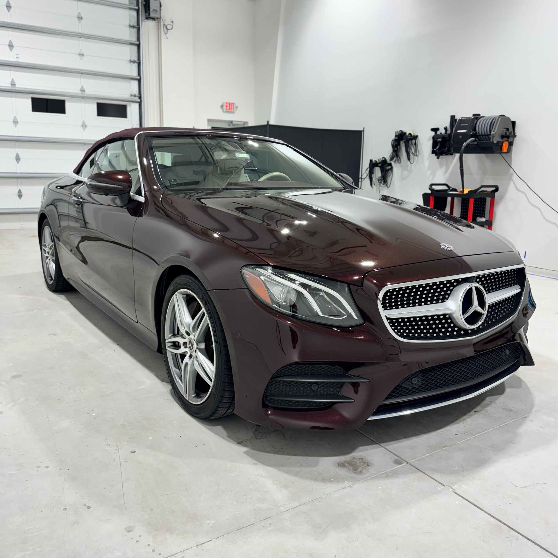 Burgundy Mercedes convertible in a well-lit garage, front view.