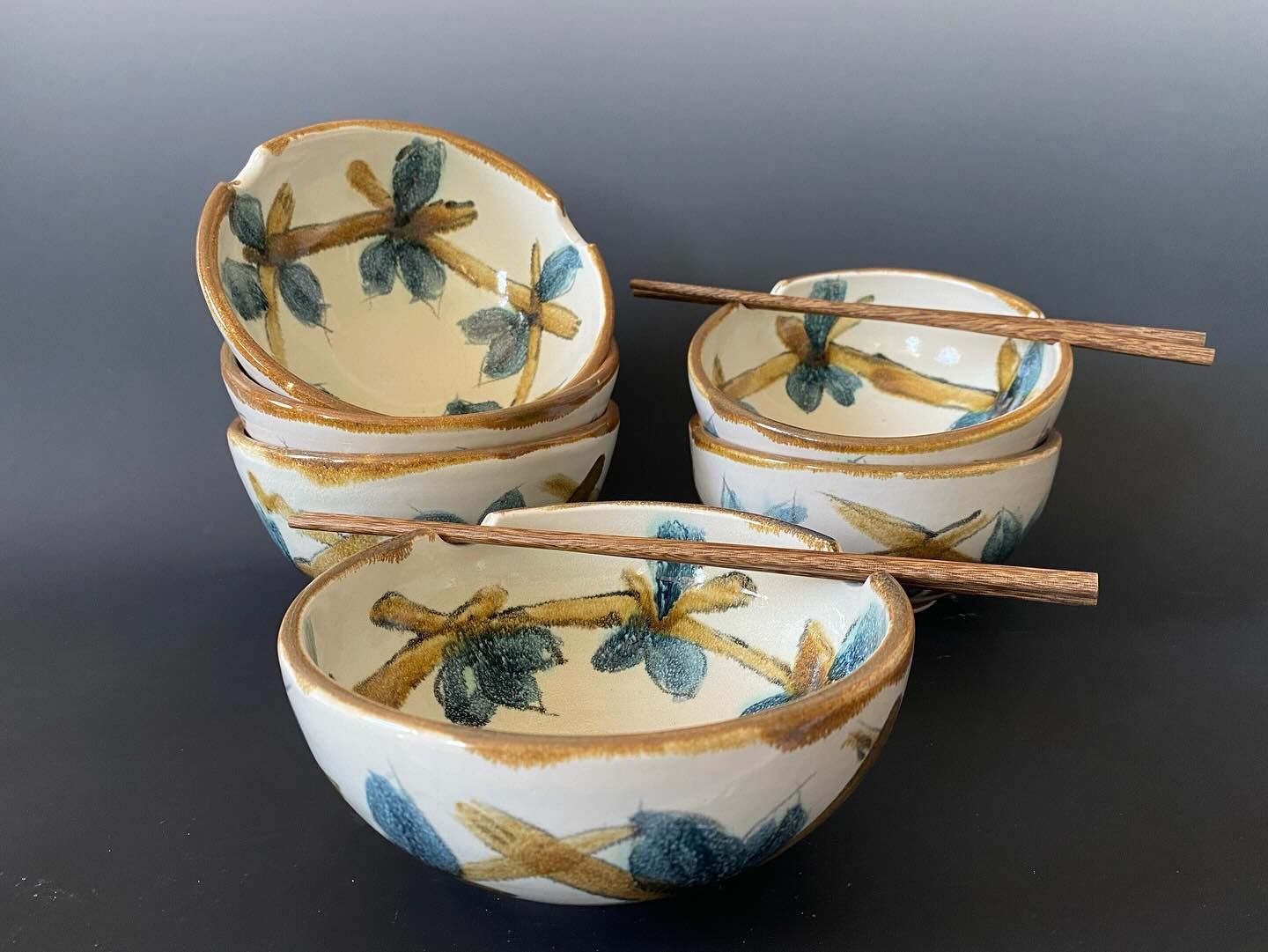 Stack of handmade ceramic bowls with blue and yellow floral design, and chopsticks.
