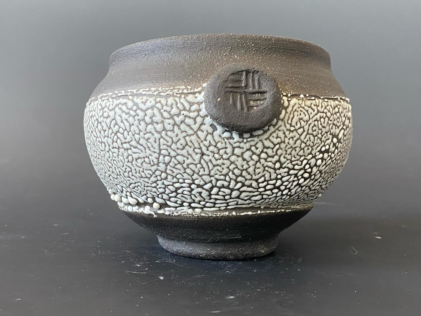 A ceramic bowl with a textured white and black glaze, and a circular design on the side.