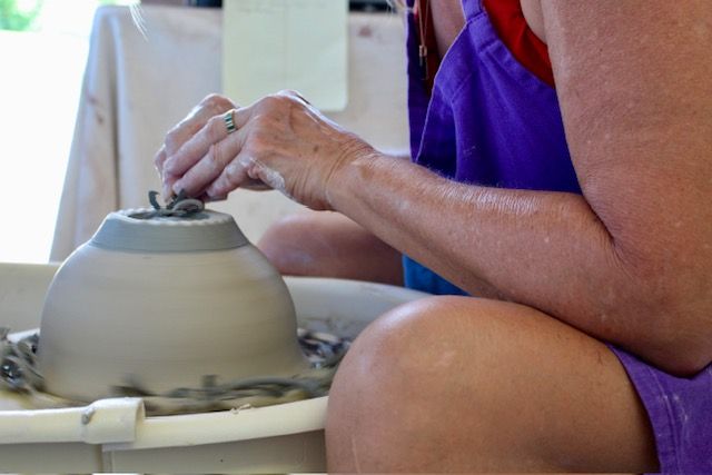 Hands shaping a clay pot on a pottery wheel, covered in wet clay.