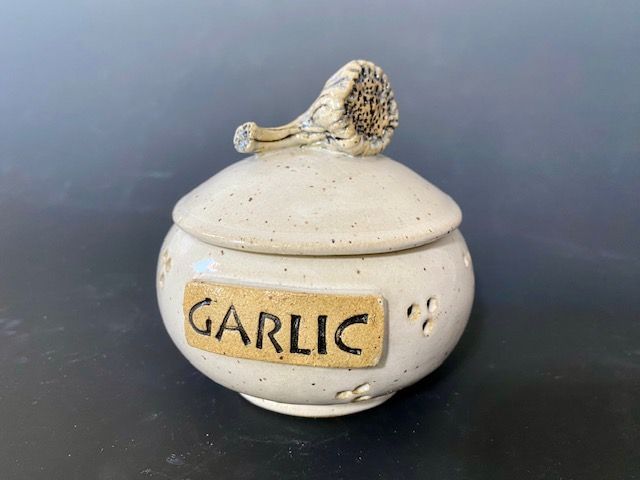 Ceramic garlic keeper with lid and garlic-shaped handle; reads