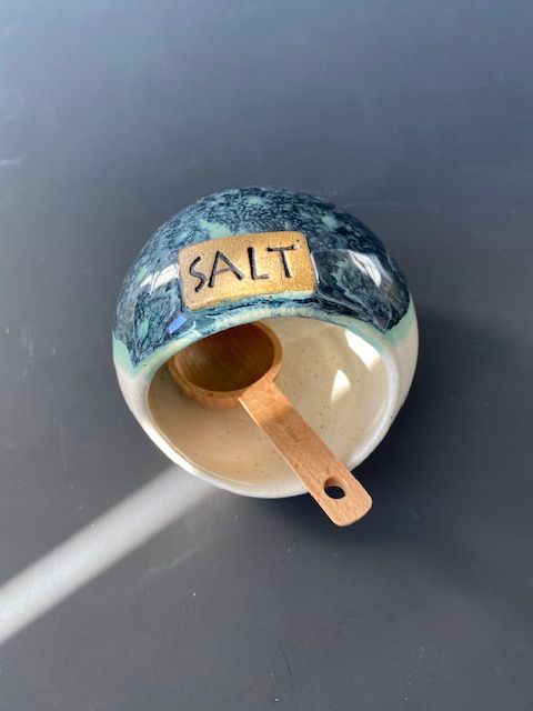 Ceramic salt cellar with blue and cream glaze, holds a wooden spoon, labeled