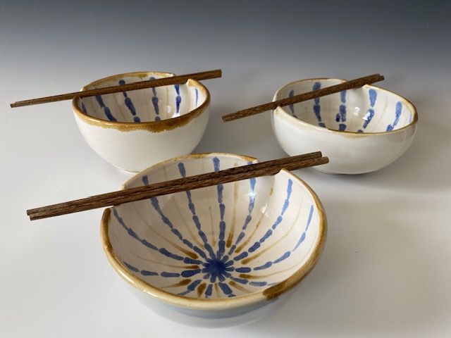 Three ceramic bowls with brown chopsticks resting on their rims; white with blue and brown interior designs.