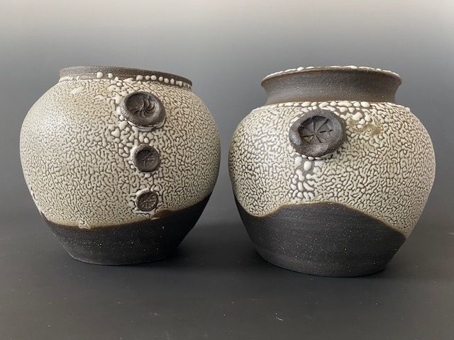 Hands covered in clay shaping a pottery vessel on a spinning wheel.