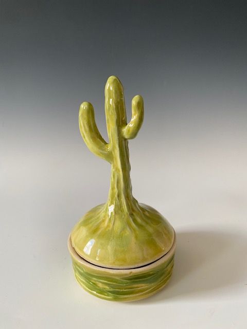 Ceramic cactus-shaped container, green and yellow glaze, on a white surface.