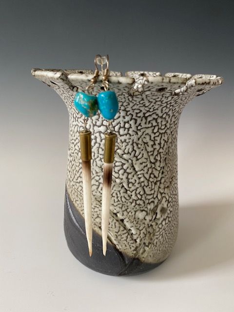 Ceramic vessel with turquoise earrings, ivory-colored bone-like sticks, speckled glaze, and dark base.