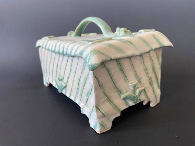 Ceramic box with green striped design, handle, and decorative accents on a gray surface.