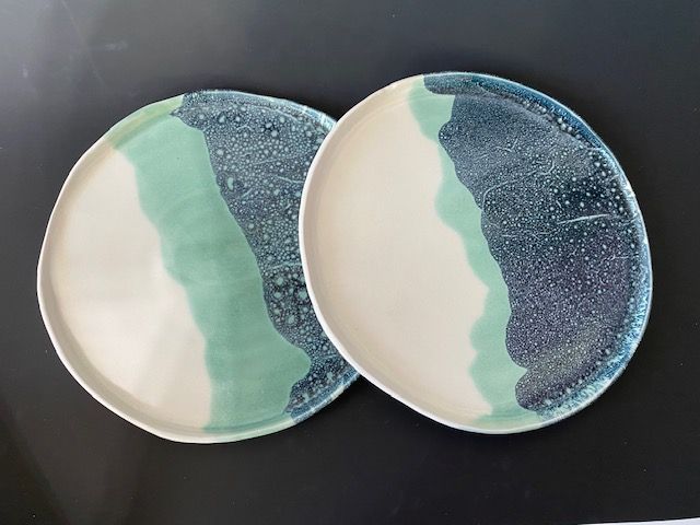 Two ceramic plates with a blue, green, and white watercolor design on a dark background.