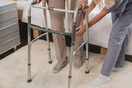 A nurse is helping an elderly woman use a walker.