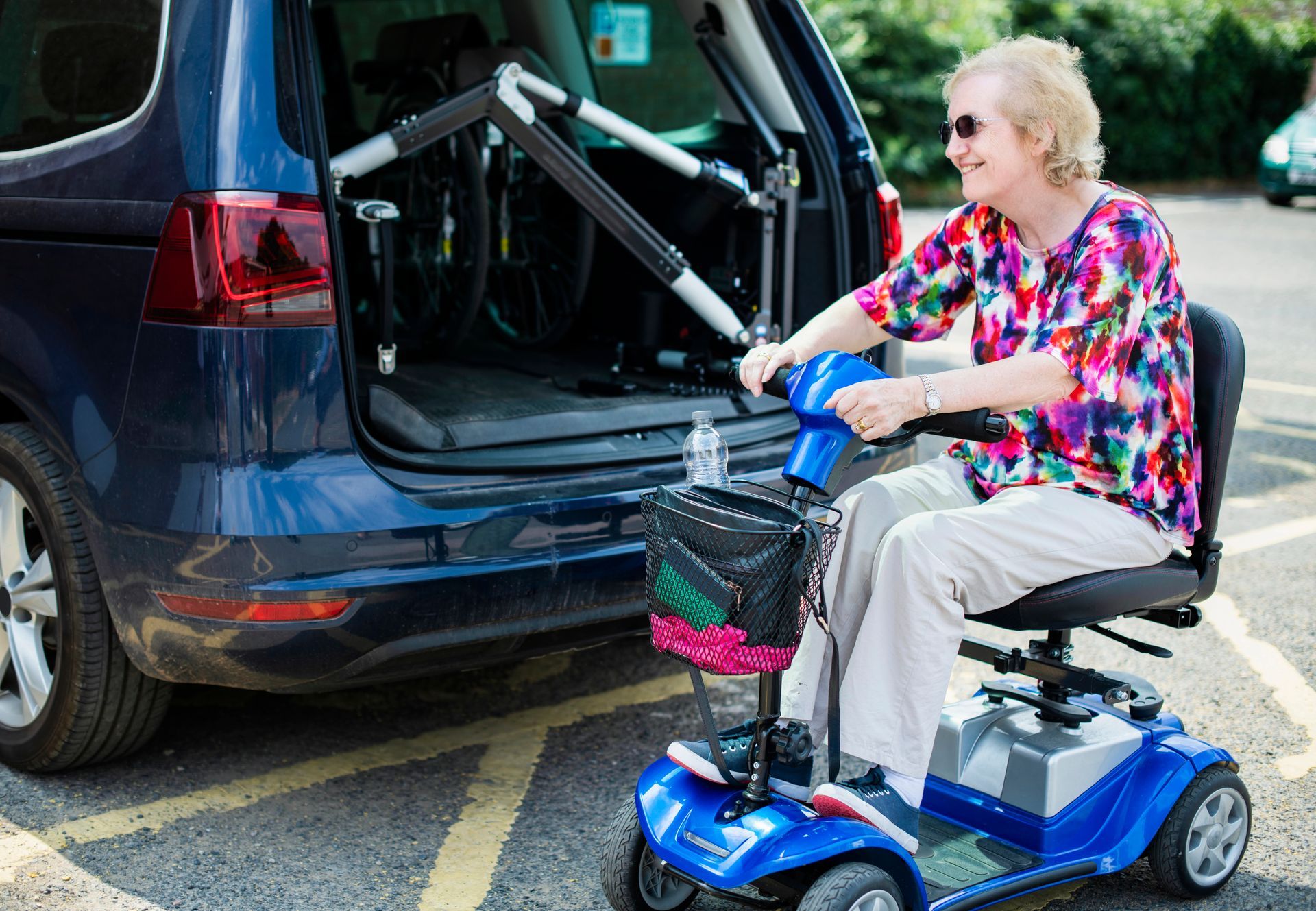 A woman is sitting on a mobility scooter in front of a car.