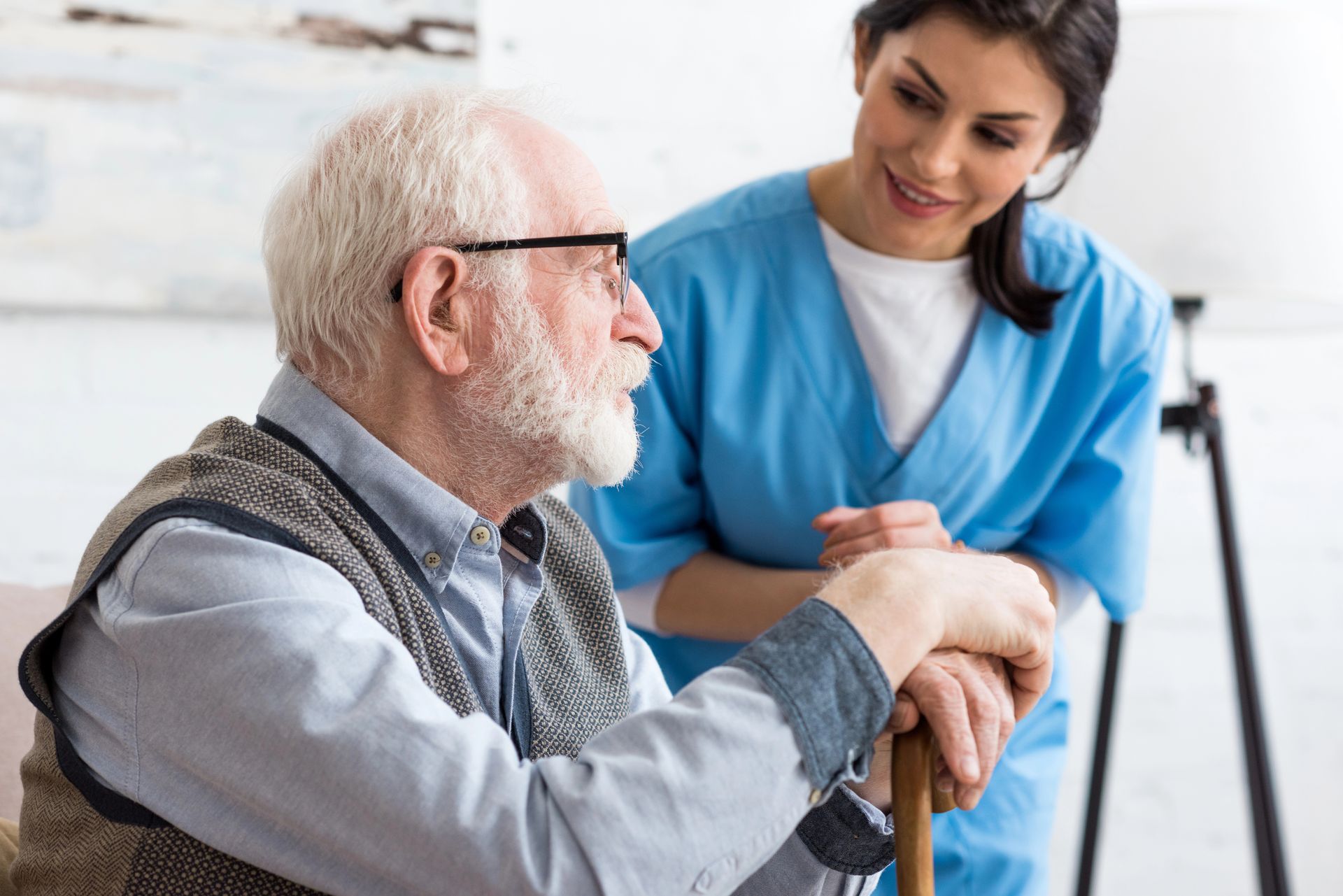 An elderly man with a cane is sitting next to a nurse.