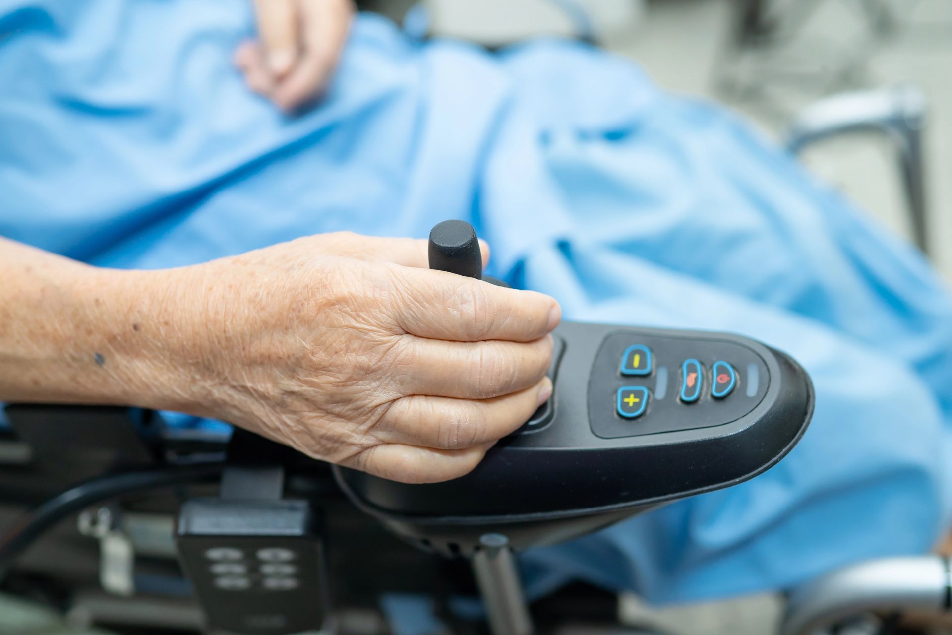 An elderly woman is sitting in an electric wheelchair holding a remote control.