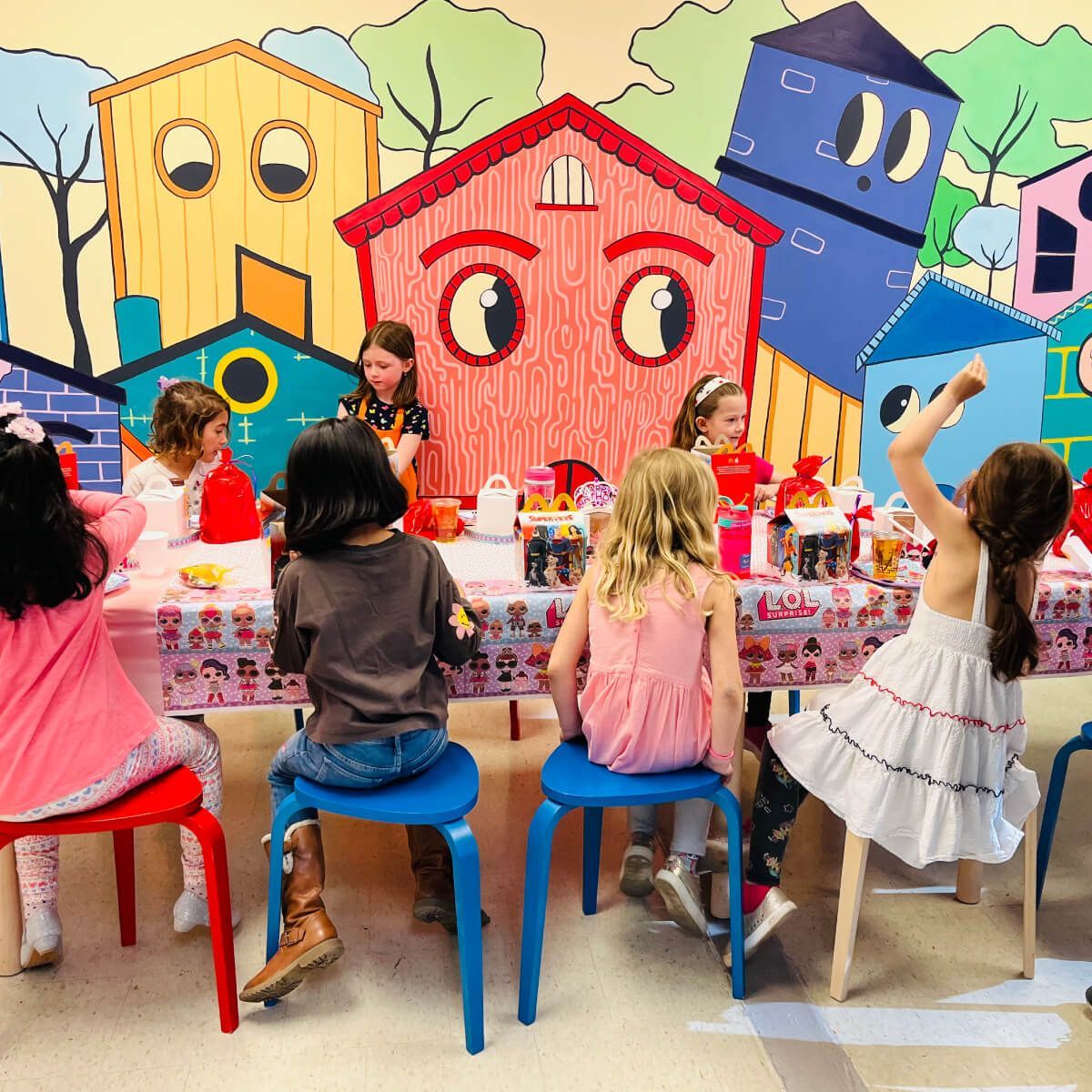 Children at a table, faces of buildings in the background.