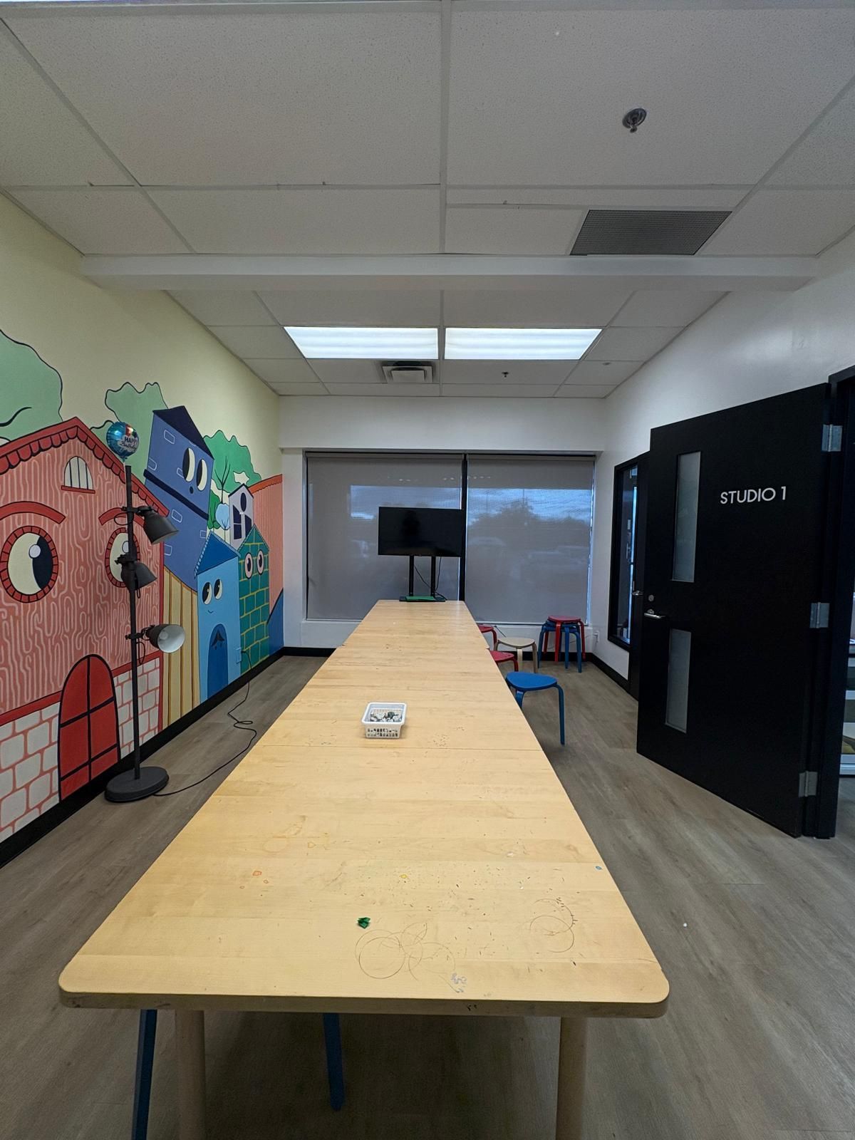 Long wooden table in a room with mural, window, and black door.