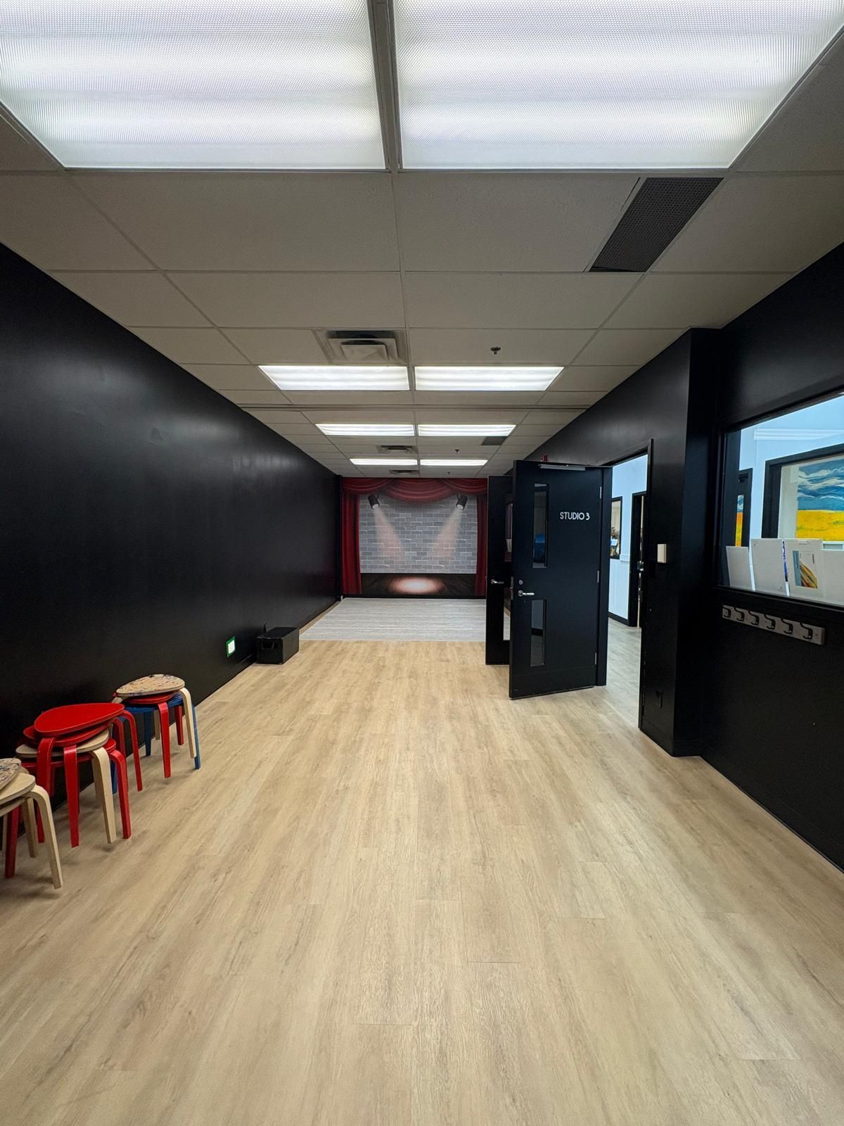 Empty dance studio with black walls, red stage, and light wood flooring.