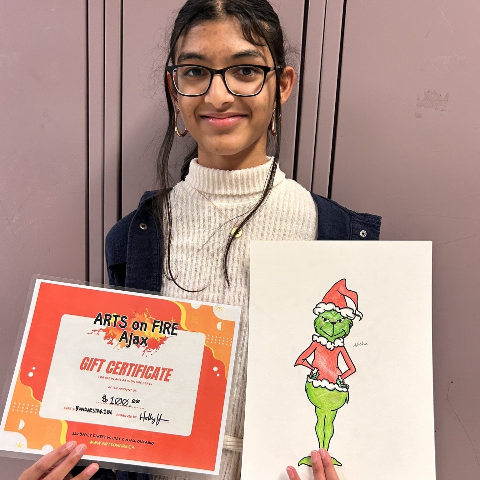 Girl holding a gift certificate and drawing of the Grinch, smiling.